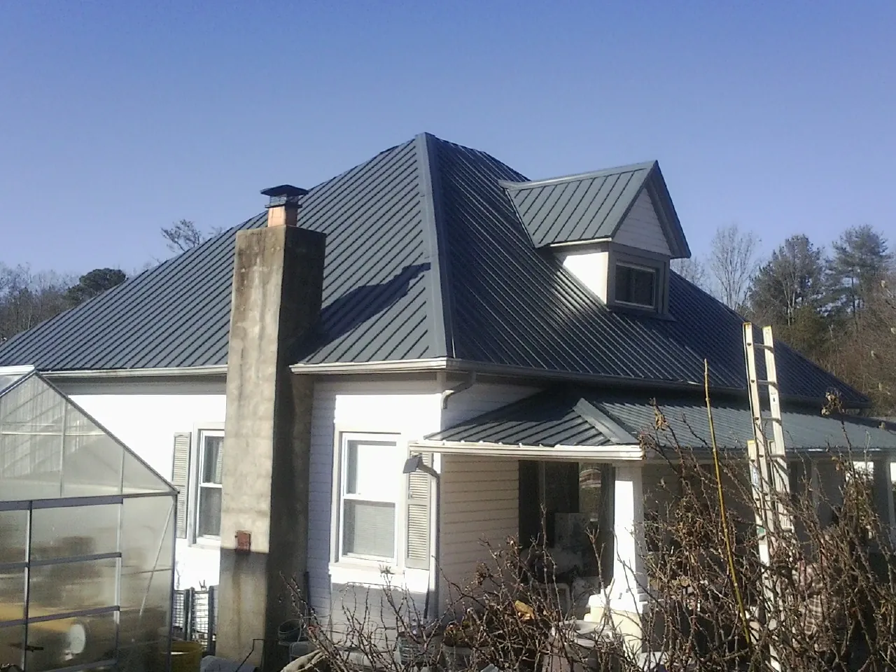 Dark blue standing seam metal roof on a white farmhouse with dormer — Slate & Tile Roof Repair by Roofing Brothers in Western