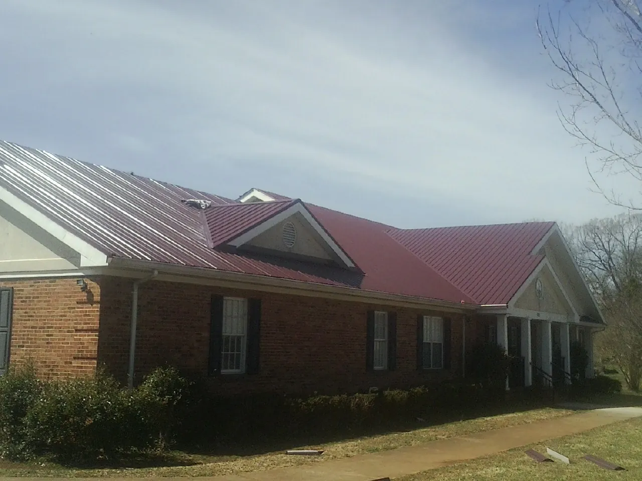 Red metal roof with gabled entries on a long brick building, from a Hail Damage Roof Repair job in Western