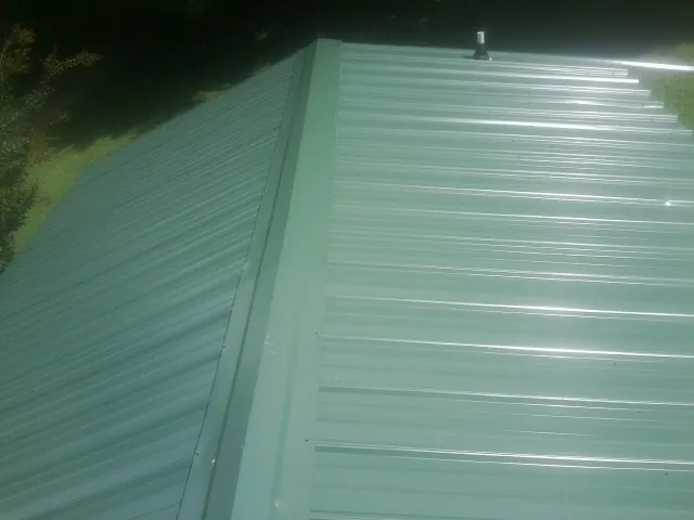 New green metal panels meeting at the ridge of a roof — Flat Roof Repair work by our crew in Western