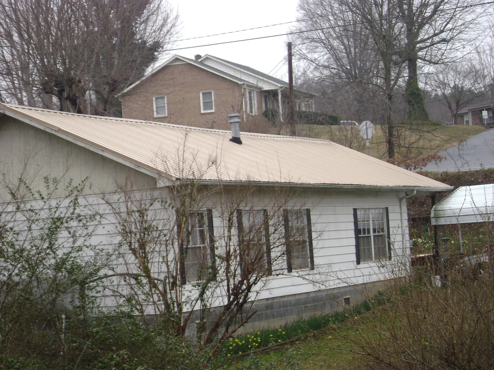 Tan metal roof on a white sided house set into a hillside — Commercial Roofing by Roofing Brothers in Western