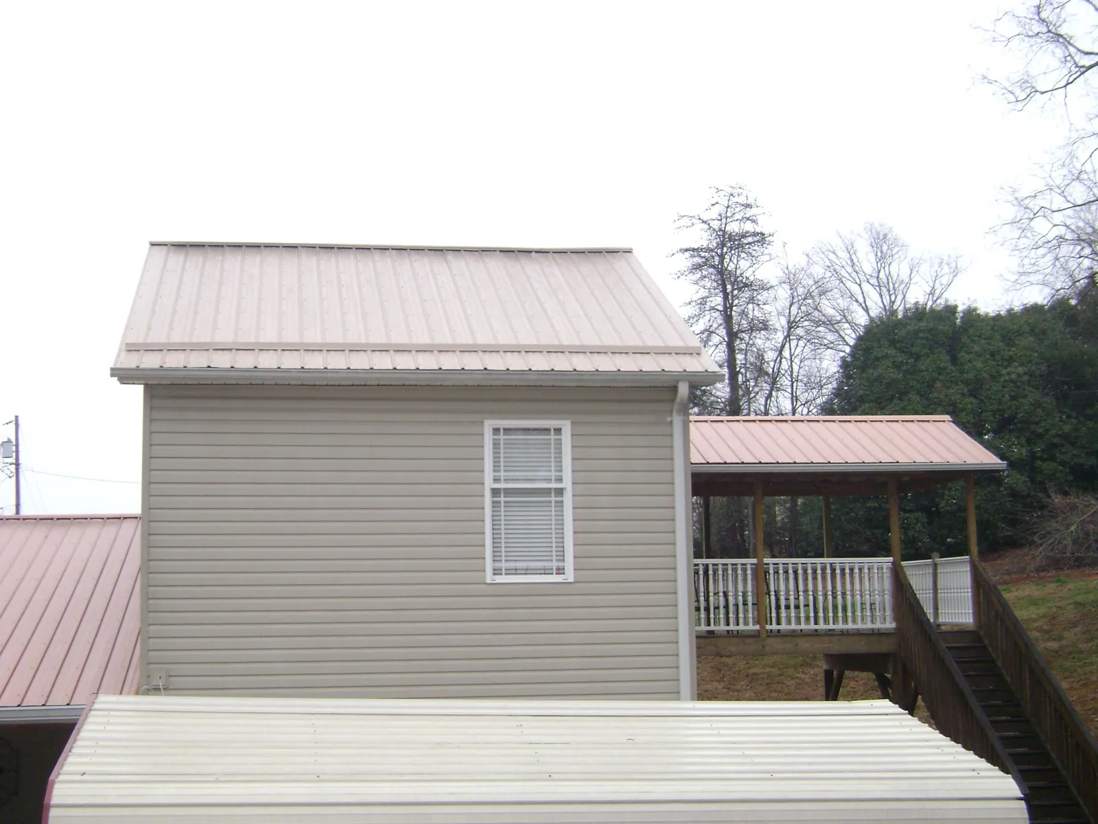 Tan metal roofs on a two story addition and attached porch, from a Roof Replacement job in Western
