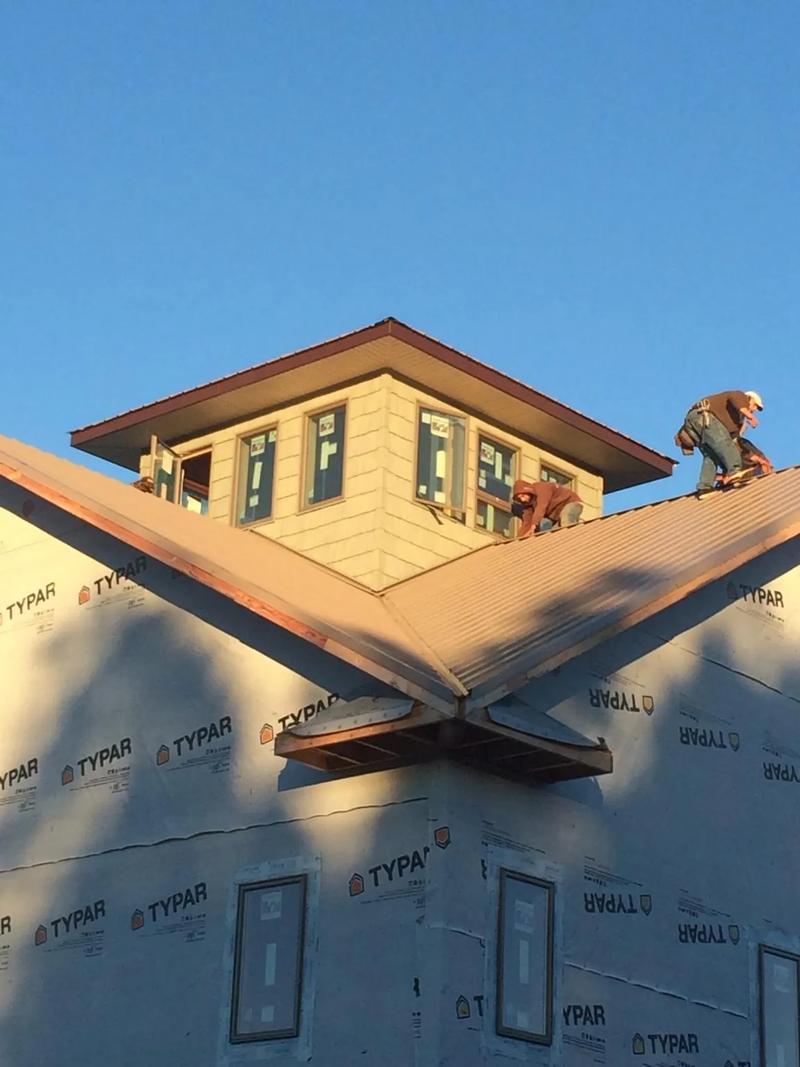 Roofers working around a rooftop cupola on a new metal roof at sunset — Roof Waterproofing in Western by Roofing Brothers